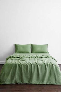 a bed with green sheets and pillows in a white room next to a wooden floor