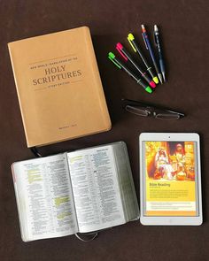 an open bible next to a tablet and some pens on a table with other items