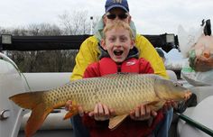 a young boy holding a large fish while sitting in a boat with another man behind him