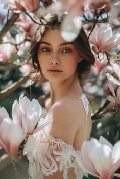 a woman standing under a tree with pink flowers in her hair and wearing a white dress