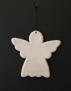 a white ceramic angel ornament hanging on a black wall with a string attached to it