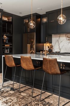 a kitchen with black cabinets and marble counter tops, gold pendant lights over the island