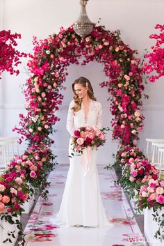 a woman standing in front of a pink flower arch with flowers around her and the words,