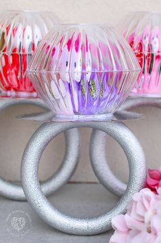 three different colored toothbrushes sitting in plastic cups on top of metal rings and flowers