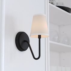 a wall light with a white shade on it's side and shelves in the background