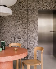 a table with two chairs and a vase on it in front of a wallpapered kitchen