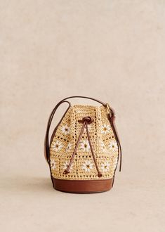 a straw bag with brown handles and white flowers on the front, sitting on a beige surface