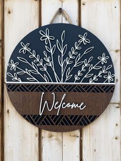 a welcome sign hanging on the side of a wooden door with flowers and leaves painted on it