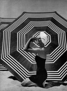 a black and white photo of a woman holding an umbrella in the sand with her hands