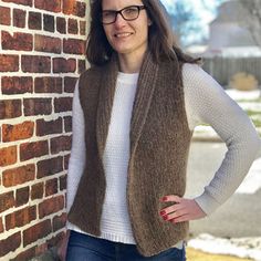 a woman leaning against a brick wall with her hands on her hips and wearing glasses