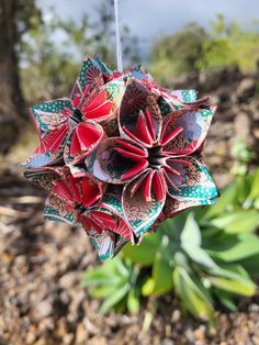 an origami flower hanging from a string in front of green plants and dirt