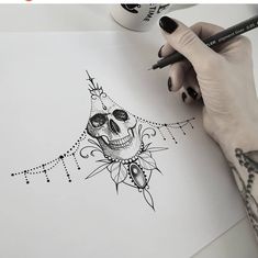 a woman's hand holding a pencil and drawing a skull with flowers on it