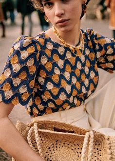 a woman is sitting on the ground with a purse in her hand and looking at the camera