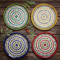 three colorful plates sitting on top of a wooden table next to leaves and berries in the background