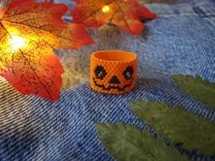 an orange bracelet with a jack - o'- lantern face on it sits next to some fall leaves