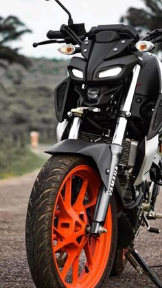 the motorcycle is parked on the side of the road with bright orange wheels and rims