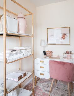 a pink chair sits in front of a white desk and gold shelving with books