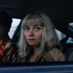 two people sitting in the back seat of a car, one looking at the camera