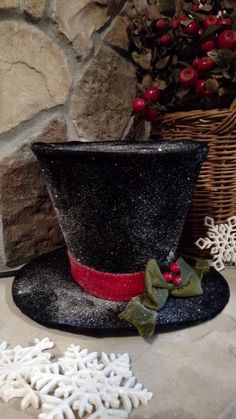 a black top hat with red trim and green bow sits next to snowflakes