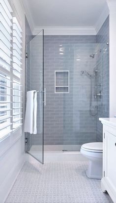 a white toilet sitting in a bathroom next to a walk in shower and window covered with blinds