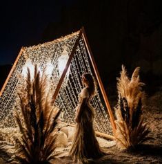 a woman is standing in the sand near some tall grass and an object with lights on it