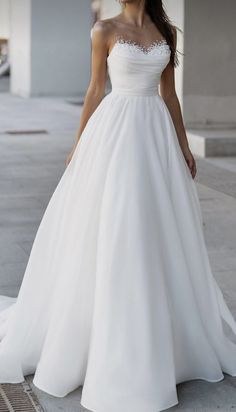 a woman in a white wedding dress standing on the sidewalk