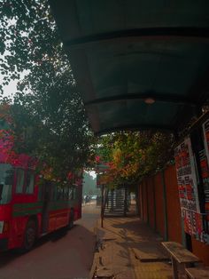 a red bus parked on the side of a road next to a tree filled with pink flowers