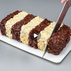 a knife cutting into a cake on top of a white plate with chocolate and cream frosting