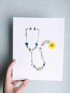 someone holding up a card with the letter s made out of watercolor flowers and daisies