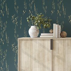 a white vase sitting on top of a wooden cabinet next to a green wallpaper