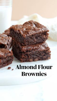 three brownies on a white plate next to a glass of milk