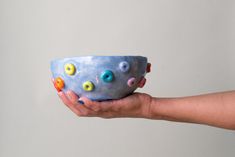 a hand holding a blue bowl with multicolored balls on it