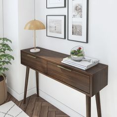 a wooden table with two pictures on the wall and a plant sitting on top of it