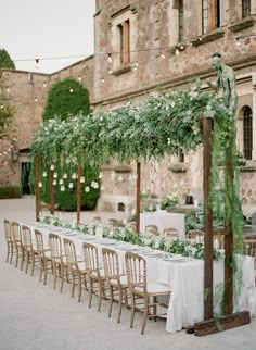 an outdoor wedding setup with white table cloths and greenery on the tables in front of a stone building