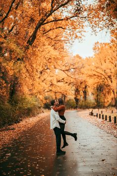 a man and woman hugging in the middle of an empty road surrounded by trees with yellow leaves