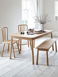 a dining table with two chairs and a bench in front of the window, next to a potted plant