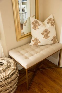 a white bench sitting in front of a mirror on top of a wooden floor next to a pillow