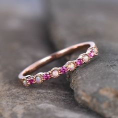 a pink and white opal ring sitting on top of a rock next to a stone