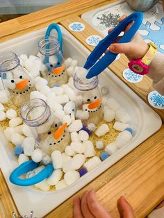 a child is making snowmen out of marshmallows and plastic bottles with scissors