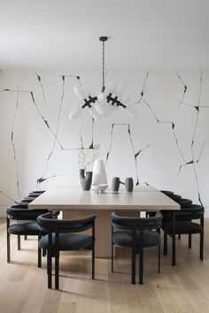 a dining room table with black chairs and vases on top of it in front of a white wall