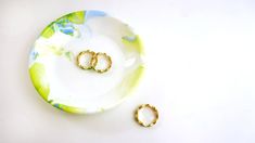 two gold rings sitting on top of a white plate next to a pair of earrings