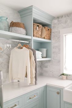 a white and blue kitchen with open shelving, baskets on the wall and sweaters hanging from hooks