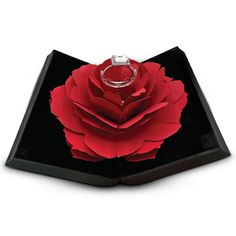 a ring sits on top of a black box with a red rose in the middle