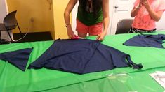 two women standing over a green table covered in blue cloth