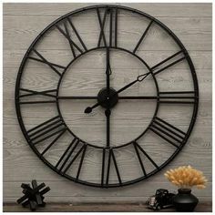 a large black clock sitting on top of a wooden table next to a vase with flowers