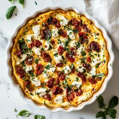 a pizza with cheese and tomatoes in a white pie dish on a marble countertop