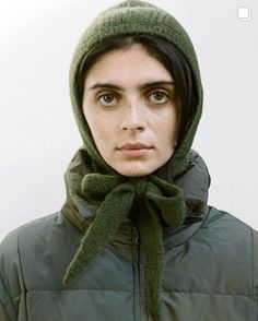 a woman wearing a green coat and a scarf around her neck is looking at the camera