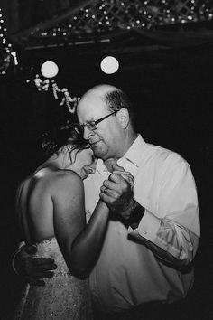 a man and woman dance together at a wedding reception in black and white photo with lights on the ceiling behind them