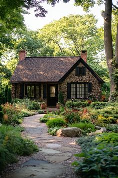 a stone house surrounded by lush green trees and flowers in the foreground is a path leading to it