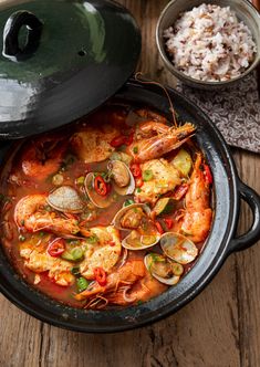 a bowl of seafood and rice on a wooden table next to a pot of rice